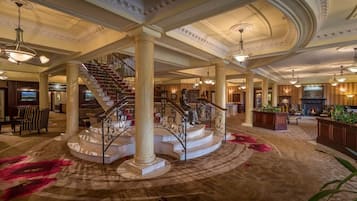 A grand lobby with a central staircase, large columns, and a fireplace.