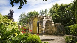 A stone structure with a wooden door, surrounded by a garden with various plants and flowers. - Slieve Russell Hotel Golf & Country Club (Ballyconnell)