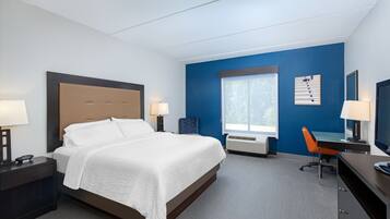 A hotel room with a bed, bedside tables, a desk, a chair, a window, and a wall-mounted TV.