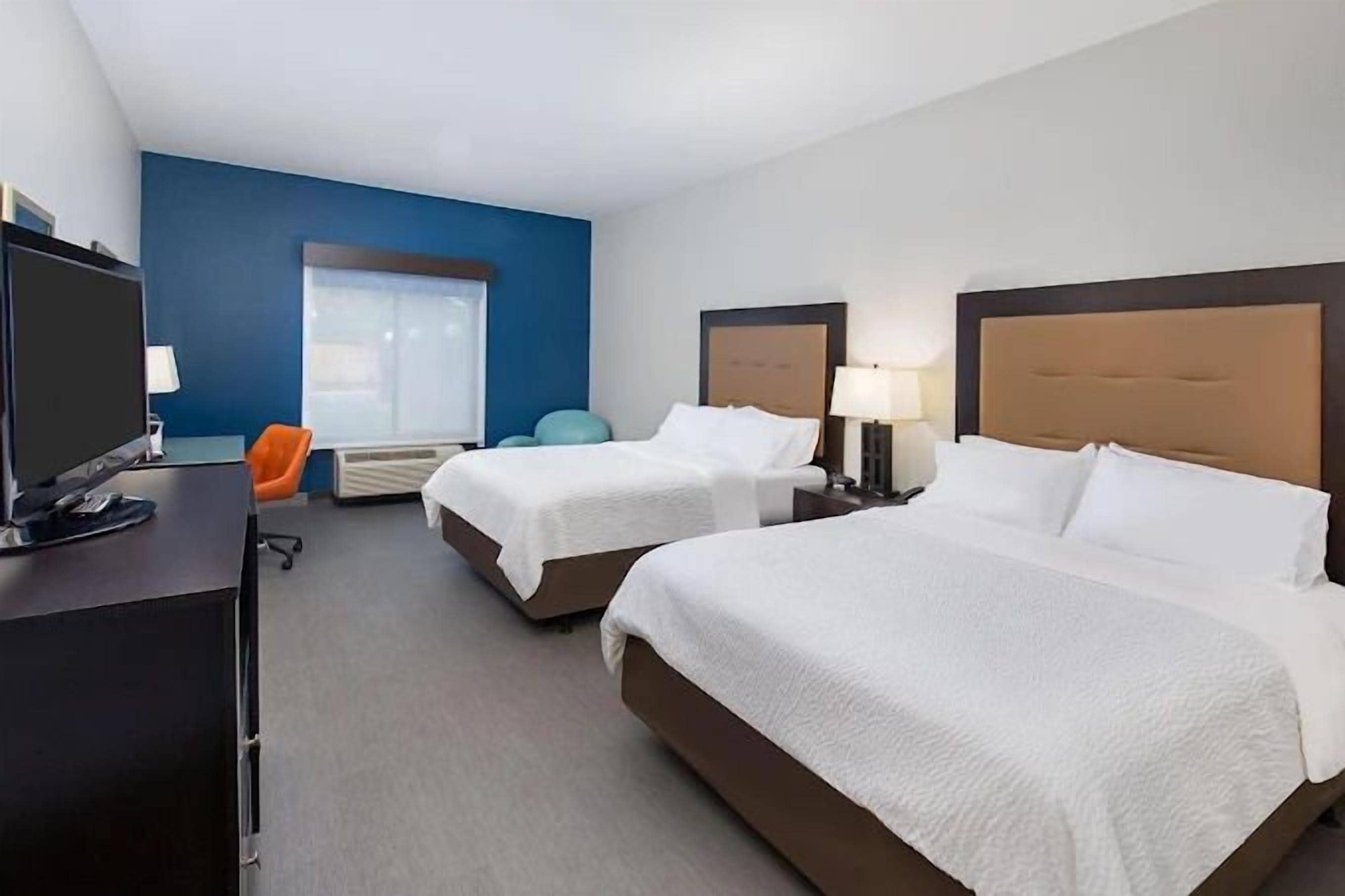 Quarto de hotel com duas camas, uma mesa com computador e uma janela.