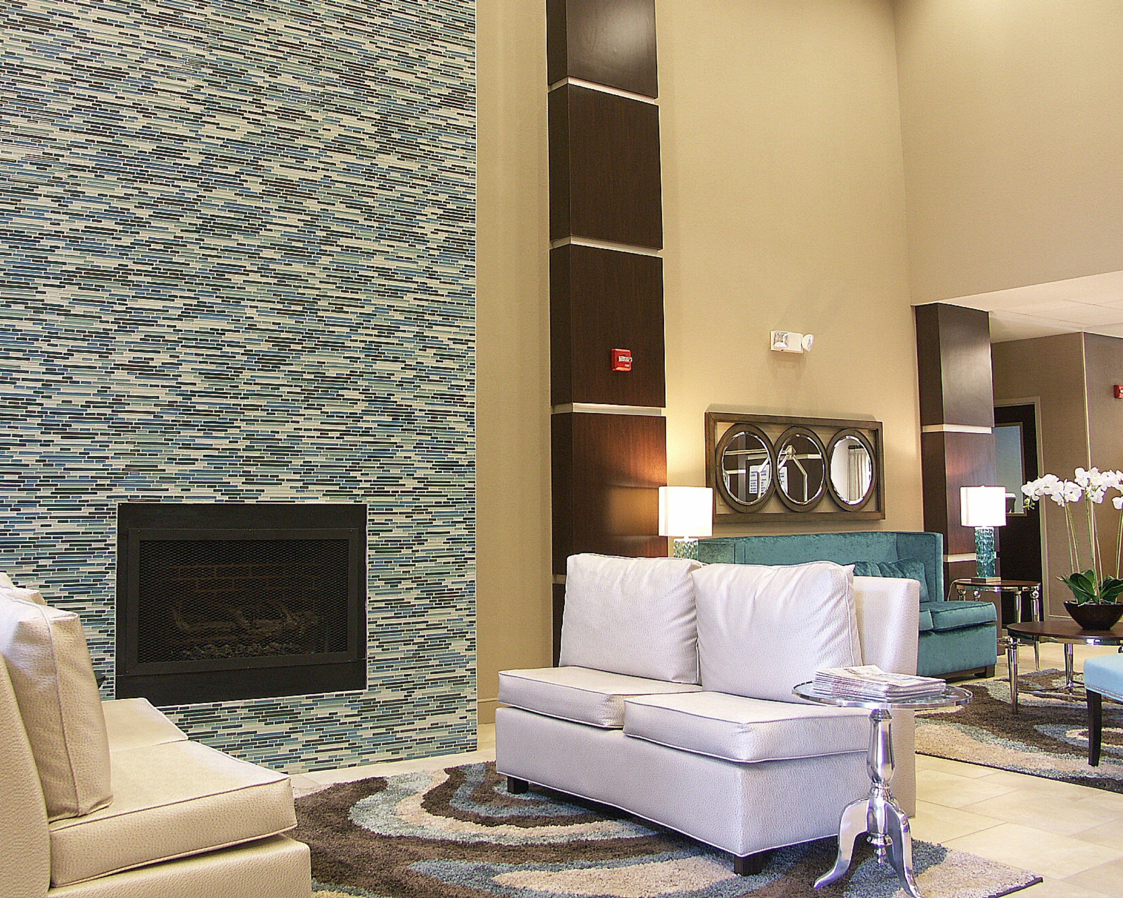 A modern lobby with a patterned wall, a fireplace, a sofa, and a decorative mirror.