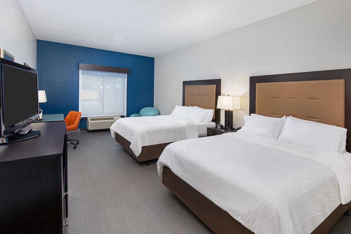 A hotel room with two beds, a desk with a computer, and a window with blinds.