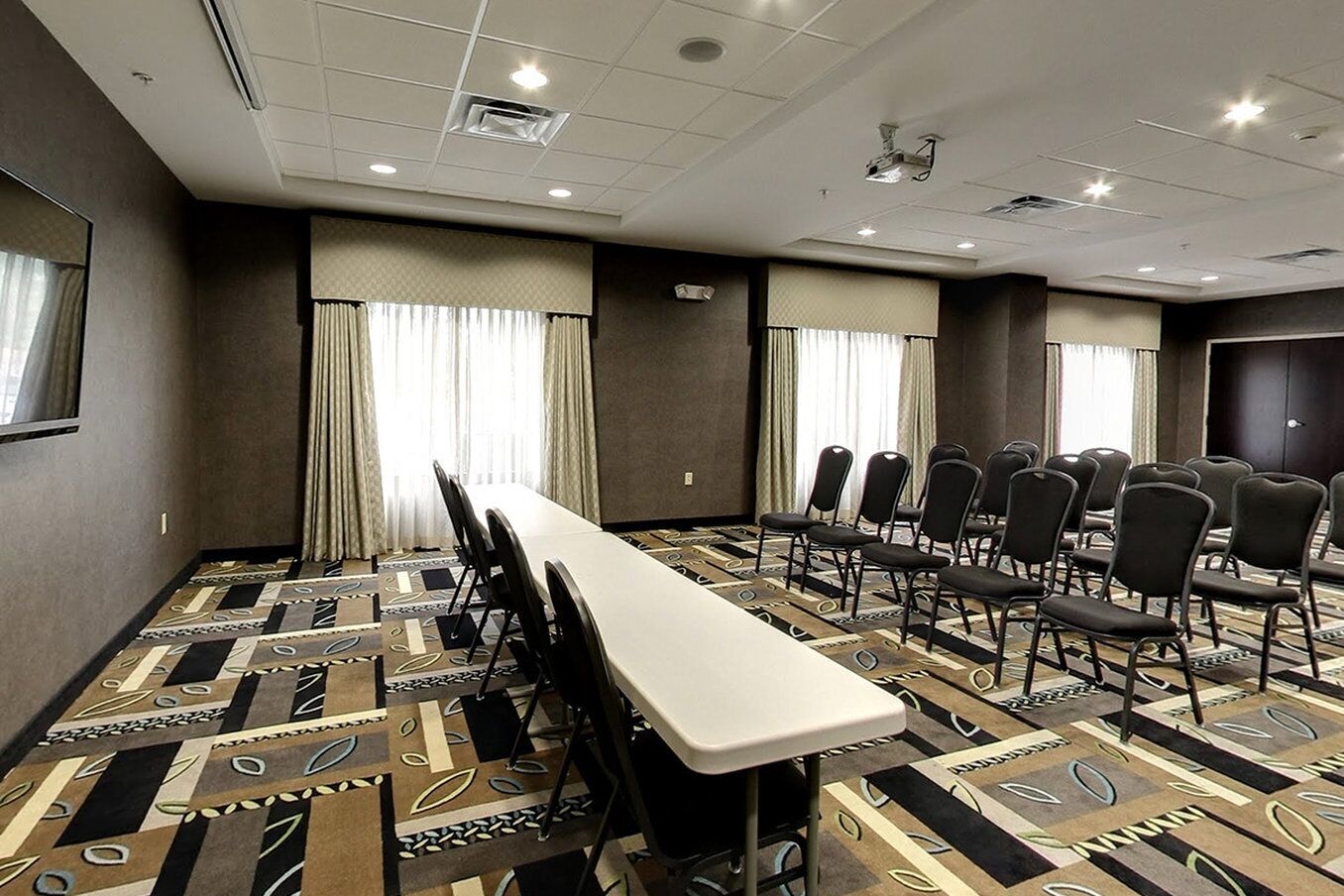 Un salón de conferencias con una larga mesa y sillas, alfombra estampada y cortinas.