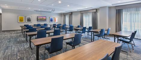 A conference room with multiple tables and chairs, large windows with curtains, and framed artwork on the walls.