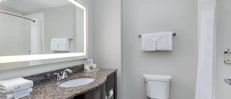 Un baño moderno con lavamanos de granito, un espejo grande, un inodoro y una zona de ducha.