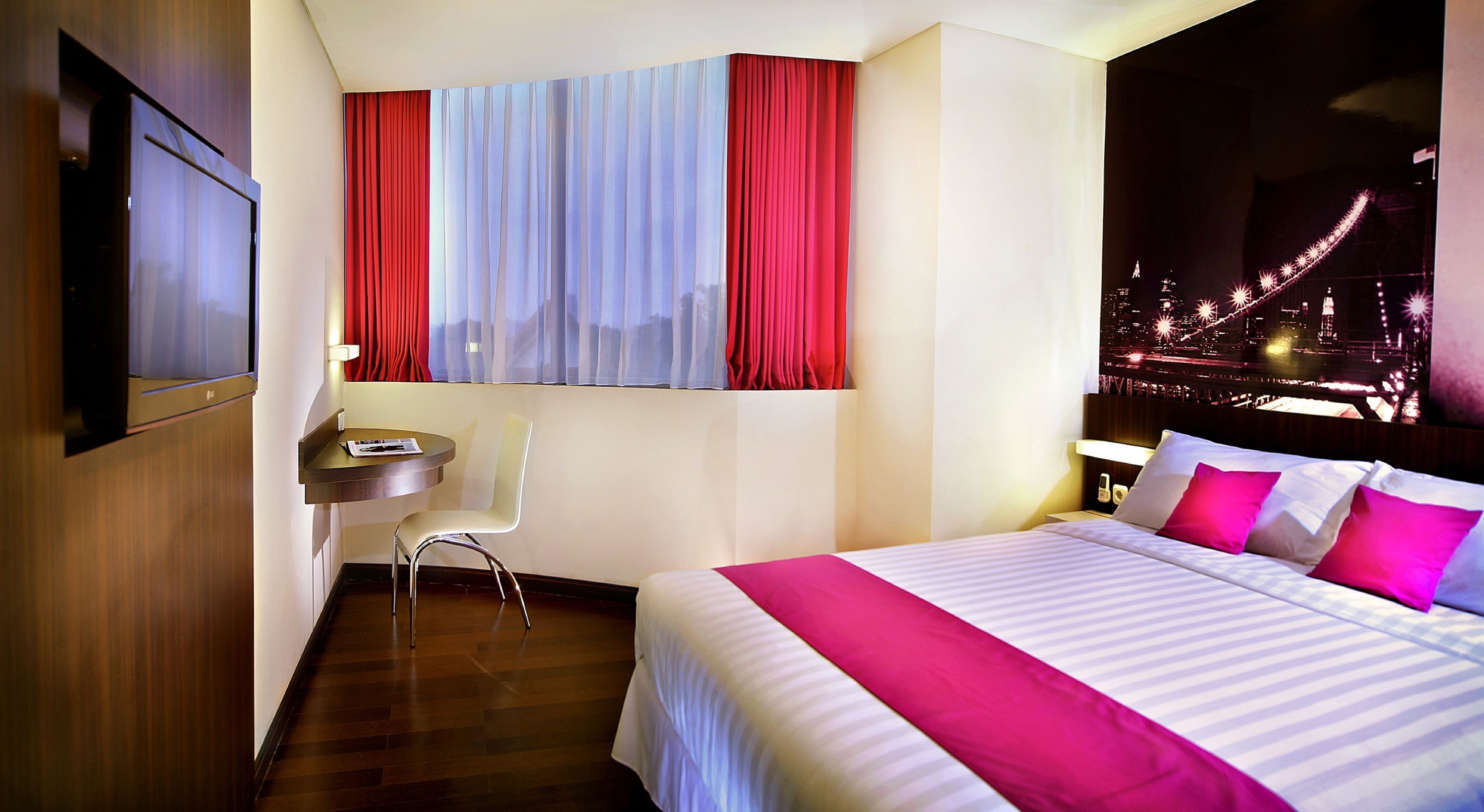 A hotel room with a bed, a desk, a chair, and a cityscape view.
