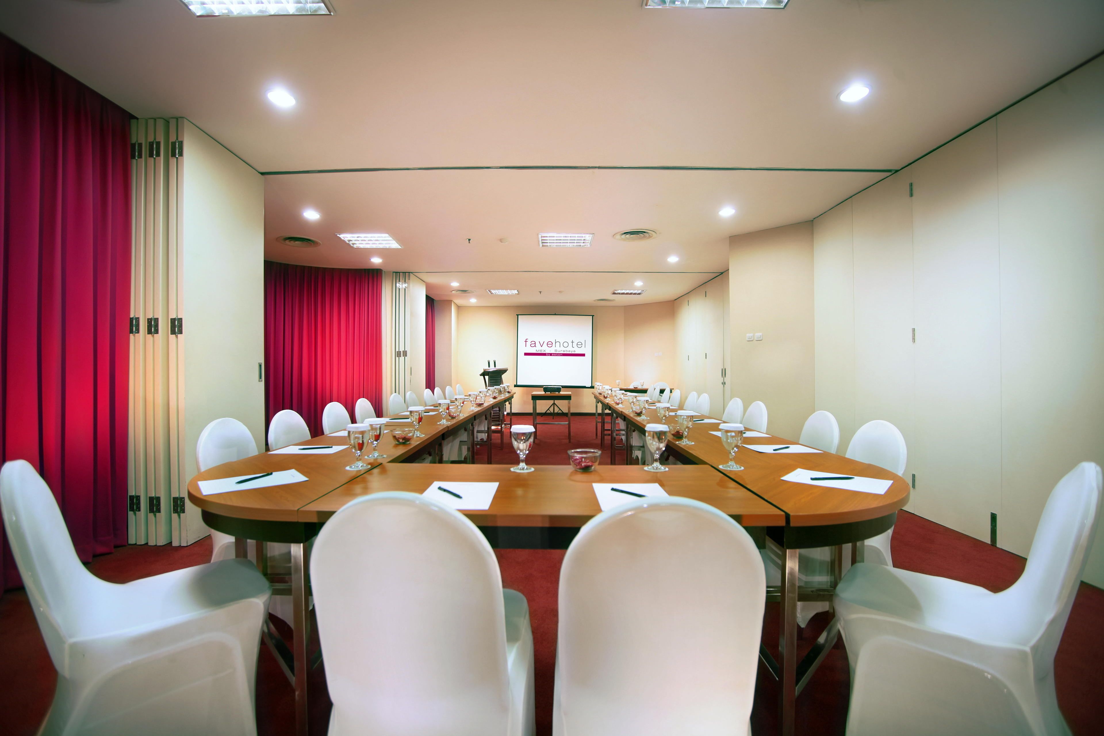 Une salle de conférence avec une longue table, des chaises blanches et un écran de présentation.