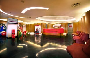 A hotel reception area with a modern design, featuring a reception desk, seating area, and a digital kiosk.