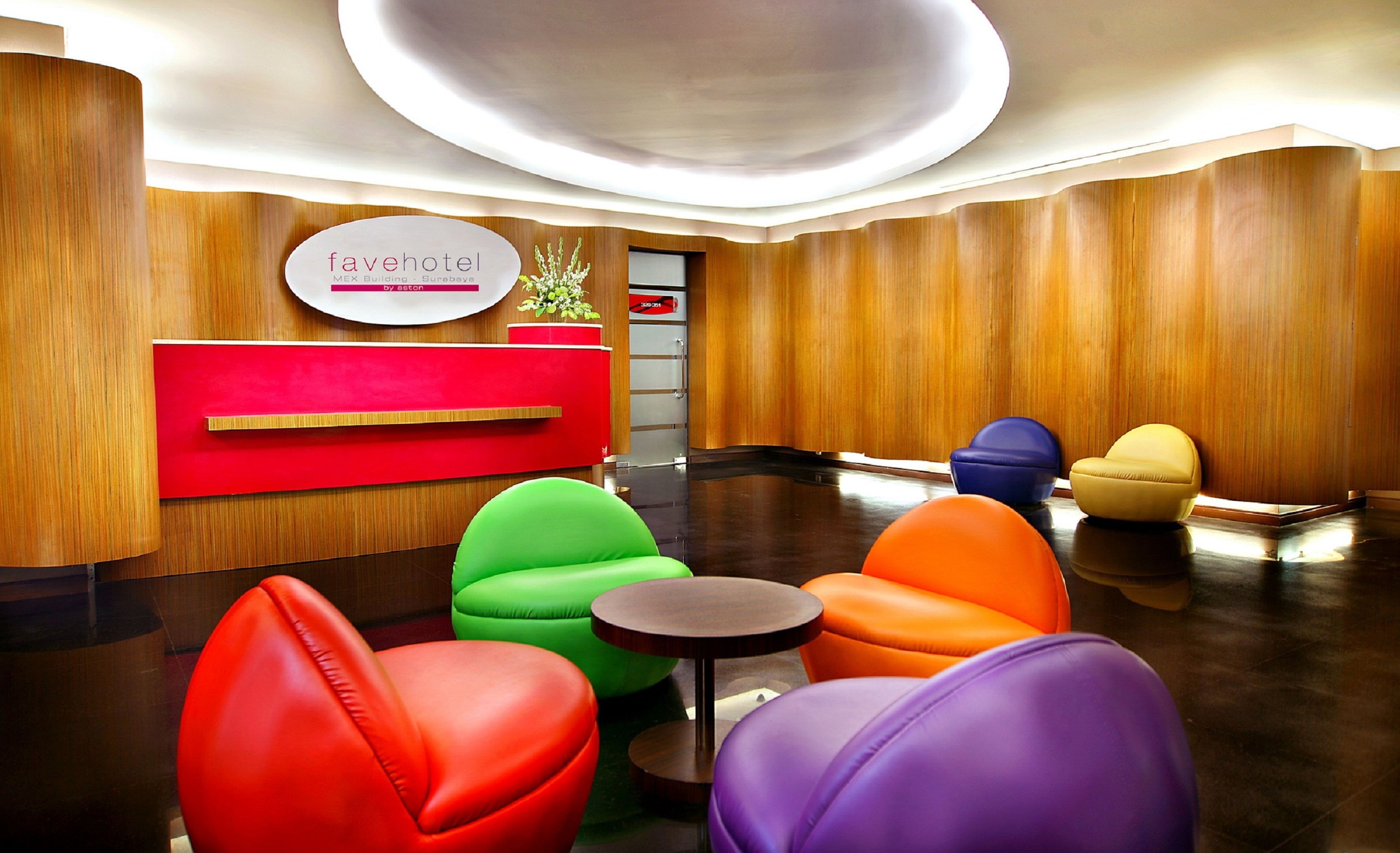 A hotel reception area with a red reception desk, colorful seating, and a wooden wall.