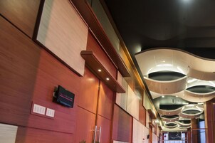 A modern hotel lobby with a wooden reception desk, a digital display, and a unique ceiling design.