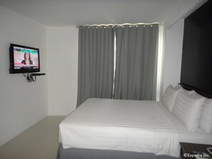 A hotel room with a bed, a television mounted on the wall, and a window with curtains. - Cityscape Hotel (Mandaue)