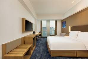 Habitación de hotel con cama, escritorio, silla y un amplio ventanal con vista a la ciudad.