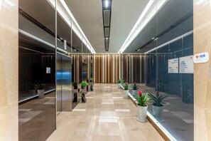A modern hotel lobby with a check-in counter, a reception desk, and a glass wall with a sign indicating amenities.