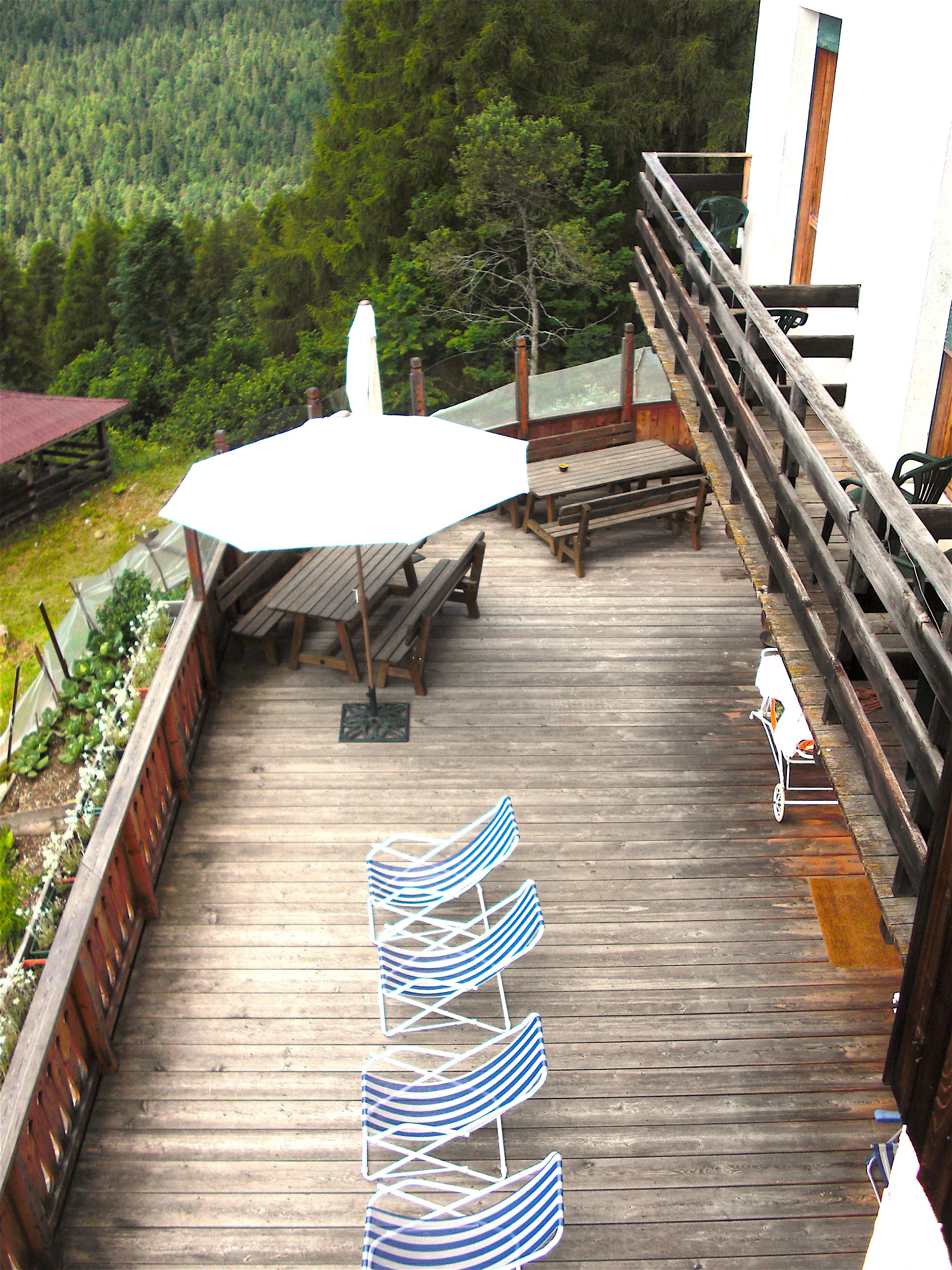 A wooden deck with picnic tables, a white umbrella, and a railing overlooking a forested area.