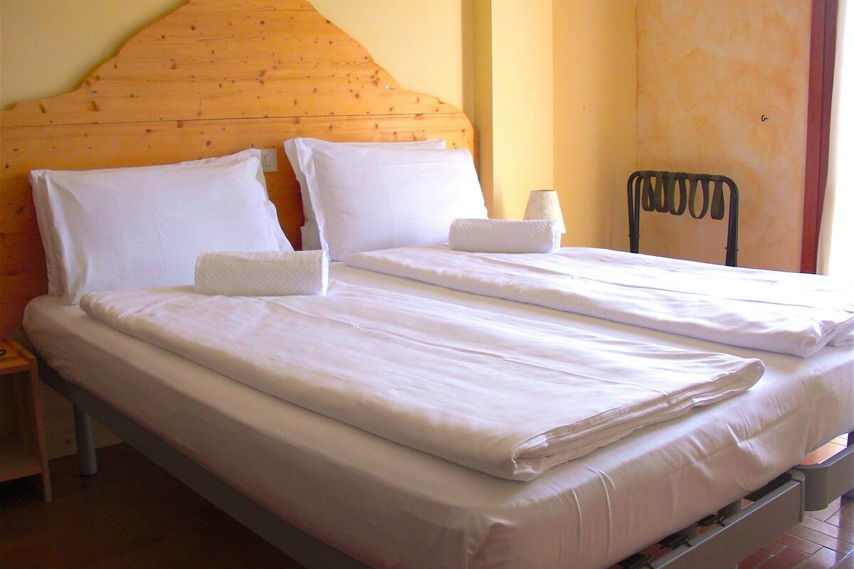 Una cama doble con ropa blanca, un cabecero de madera y una silla de metal.