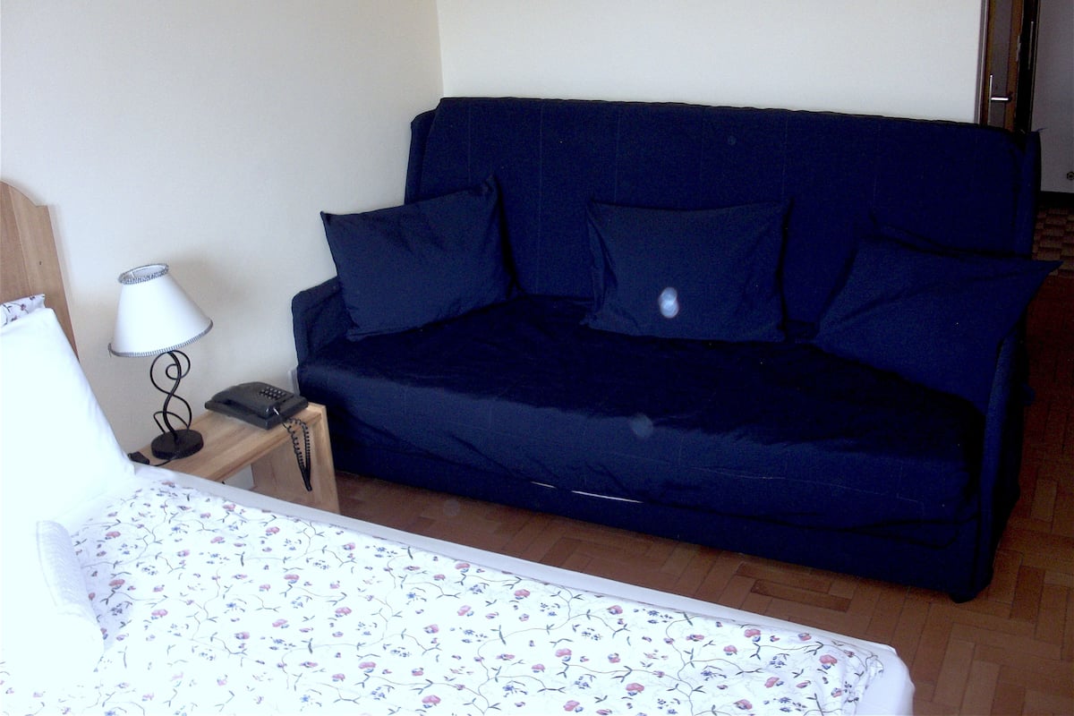 Una habitación con un sofá azul oscuro, una lámpara blanca, un teléfono y una colcha con estampado floral.