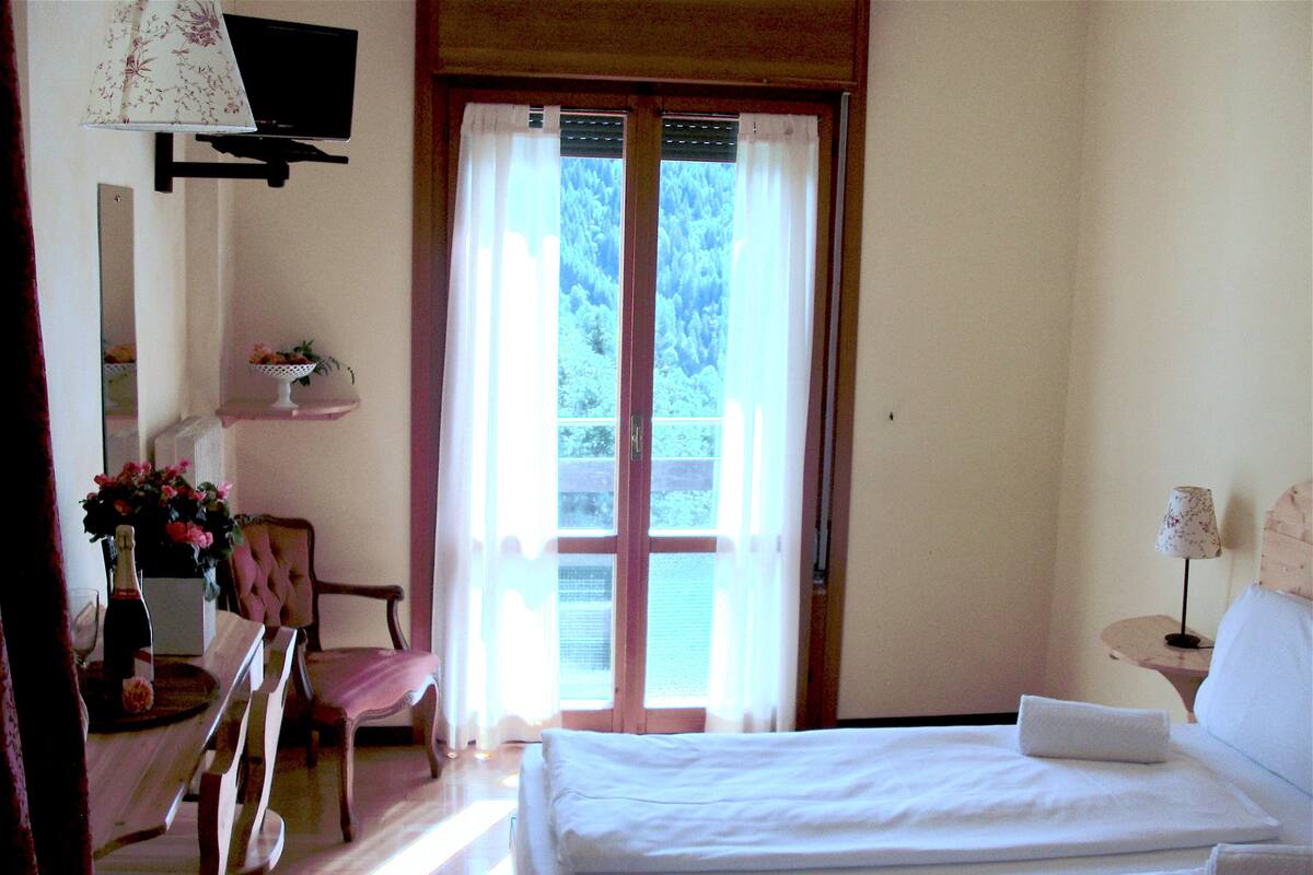 Un dormitorio con una cama, una silla, una mesa con una botella y un televisor en la pared.