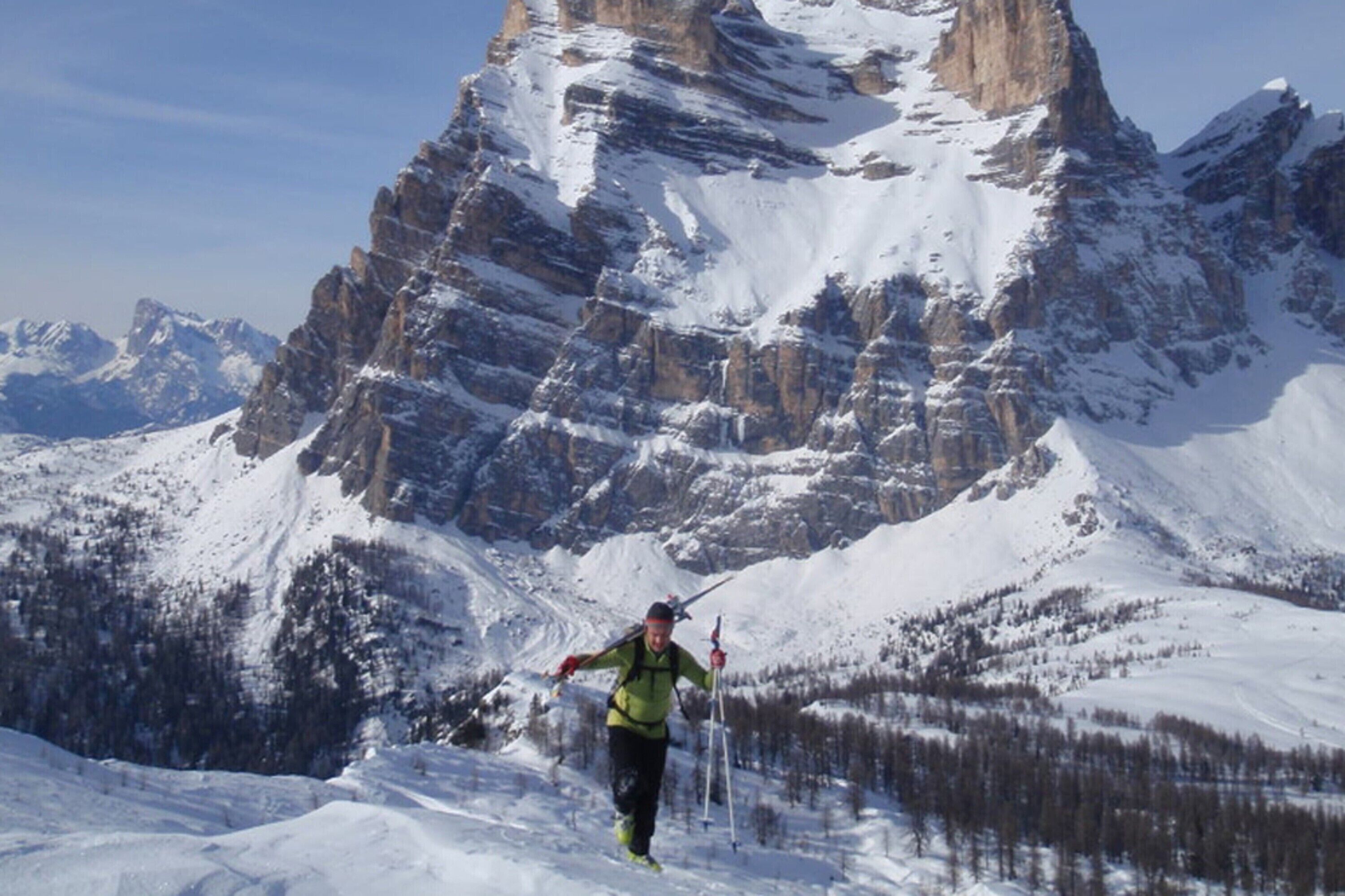 A person hiking in a snowy mountainous area with rocky terrain and trees.