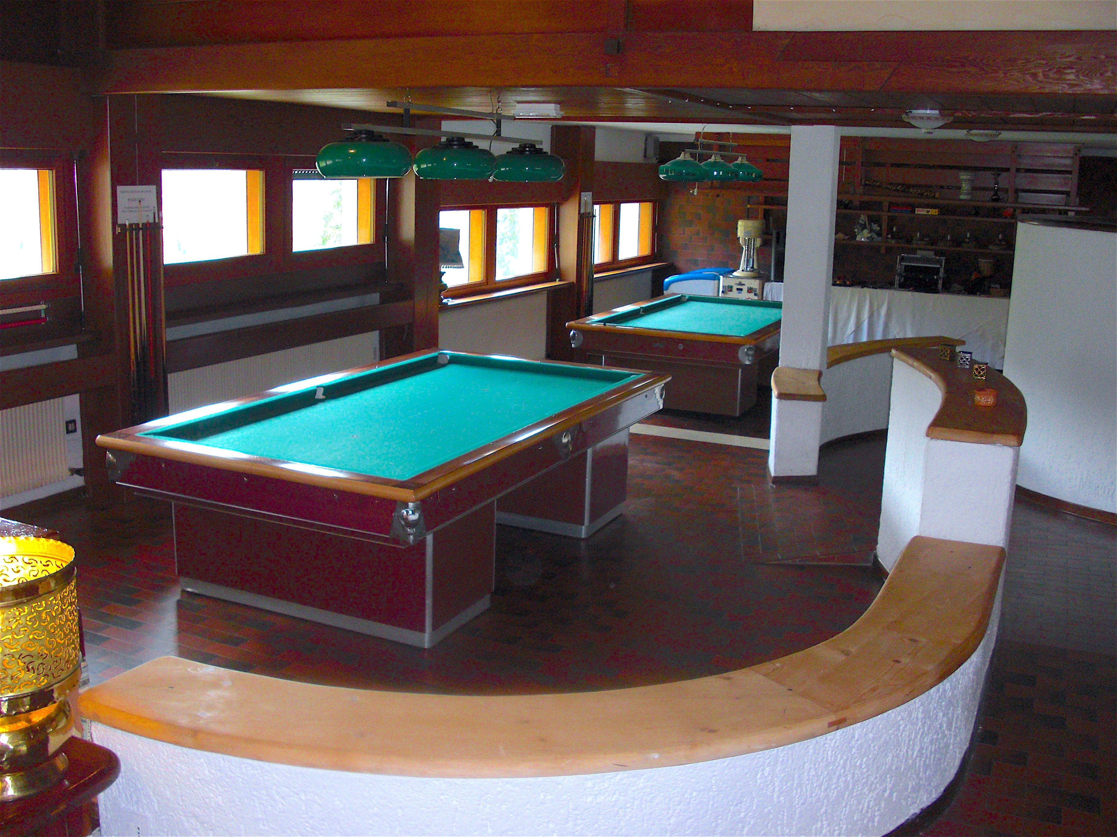 Een pooltafel in een ruimte met houten lambrisering en een gebogen witte bar.