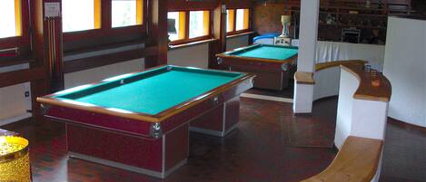 Een pooltafel in een ruimte met houten lambrisering en een gebogen witte bar.