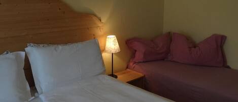 Una habitación con cama de cabecera de madera, lámpara de noche y dos camas con ropa de cama de diferentes colores.