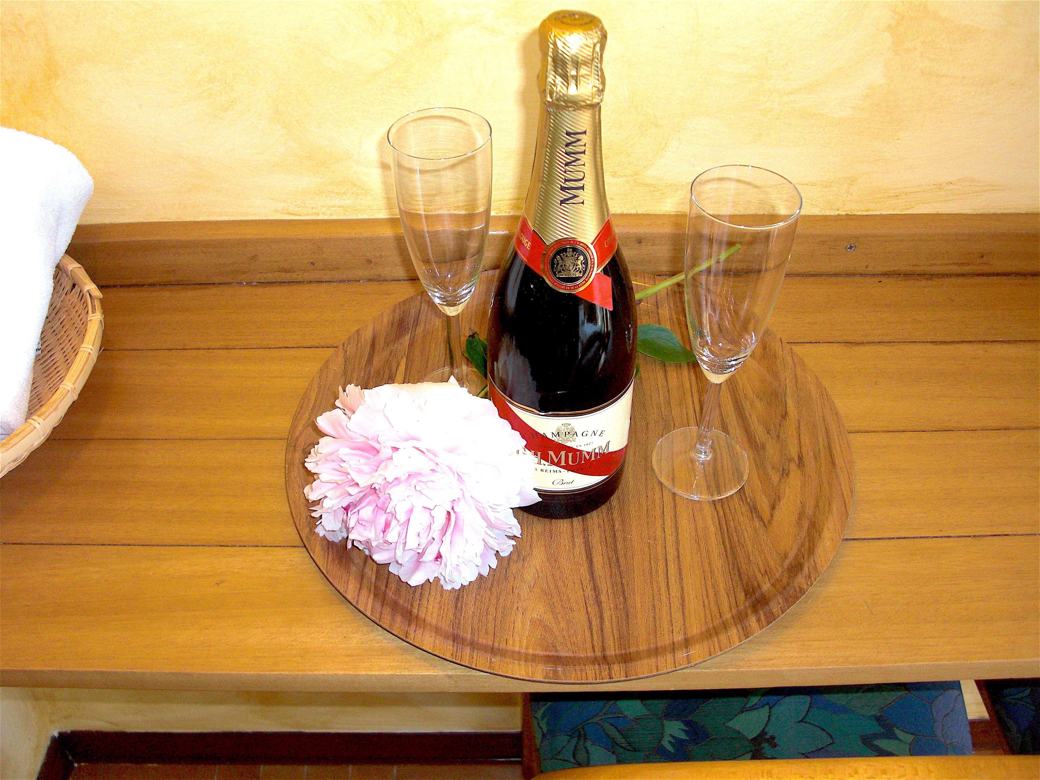 A bottle of champagne on a wooden tray with two glasses and a pink flower.