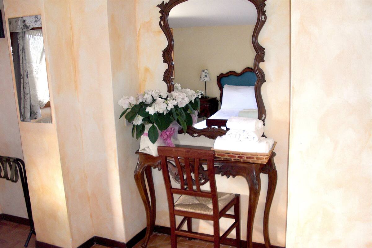 Una habitación con un escritorio de madera, una silla, un espejo y un florero con flores.