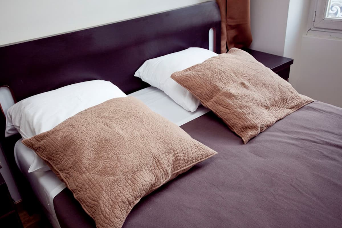 Una cama con cabecera oscura, dos almohadas blancas y dos almohadas marrones.