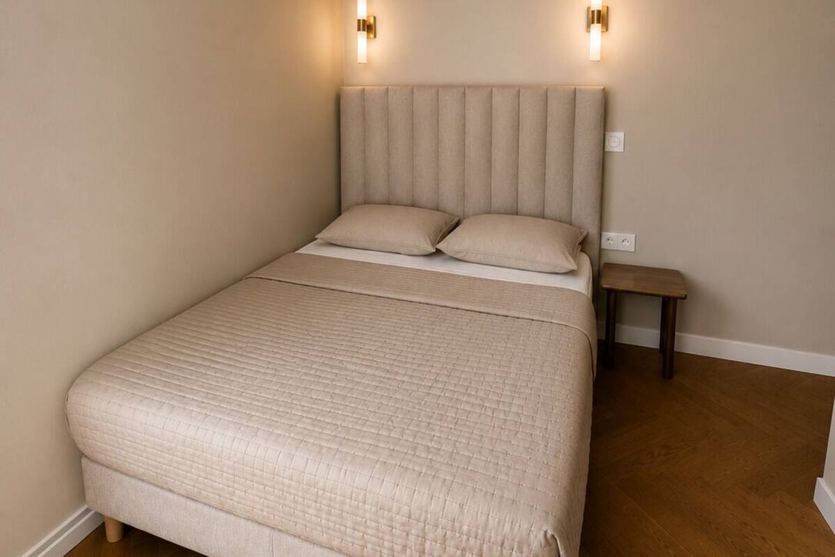 Un dormitorio con una cama grande, dos lámparas de pared, una mesita de noche y suelo de madera.