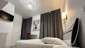 Un dormitorio moderno con cama, mesita de noche, silla, radiador y lámpara fijada a la pared.