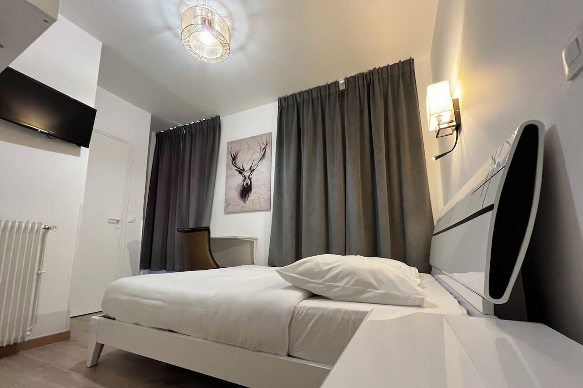 Un dormitorio moderno con cama, mesita de noche, silla, radiador y lámpara fijada a la pared.