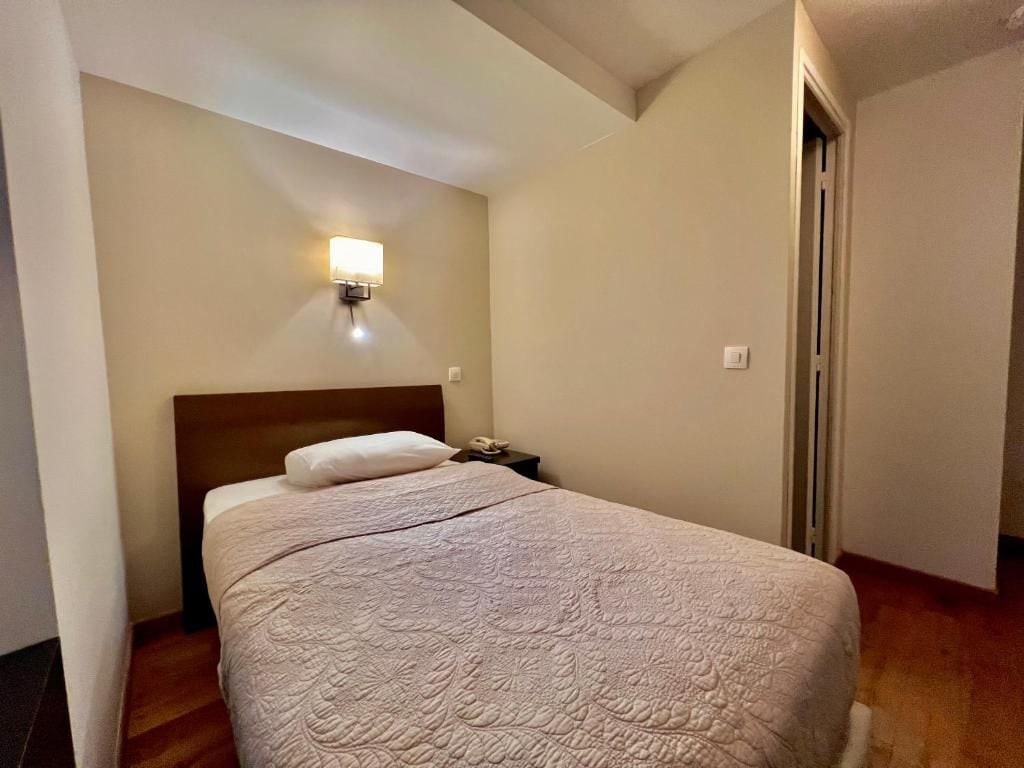Un dormitorio con cama, mesita de noche, lámpara de pared y una puerta.