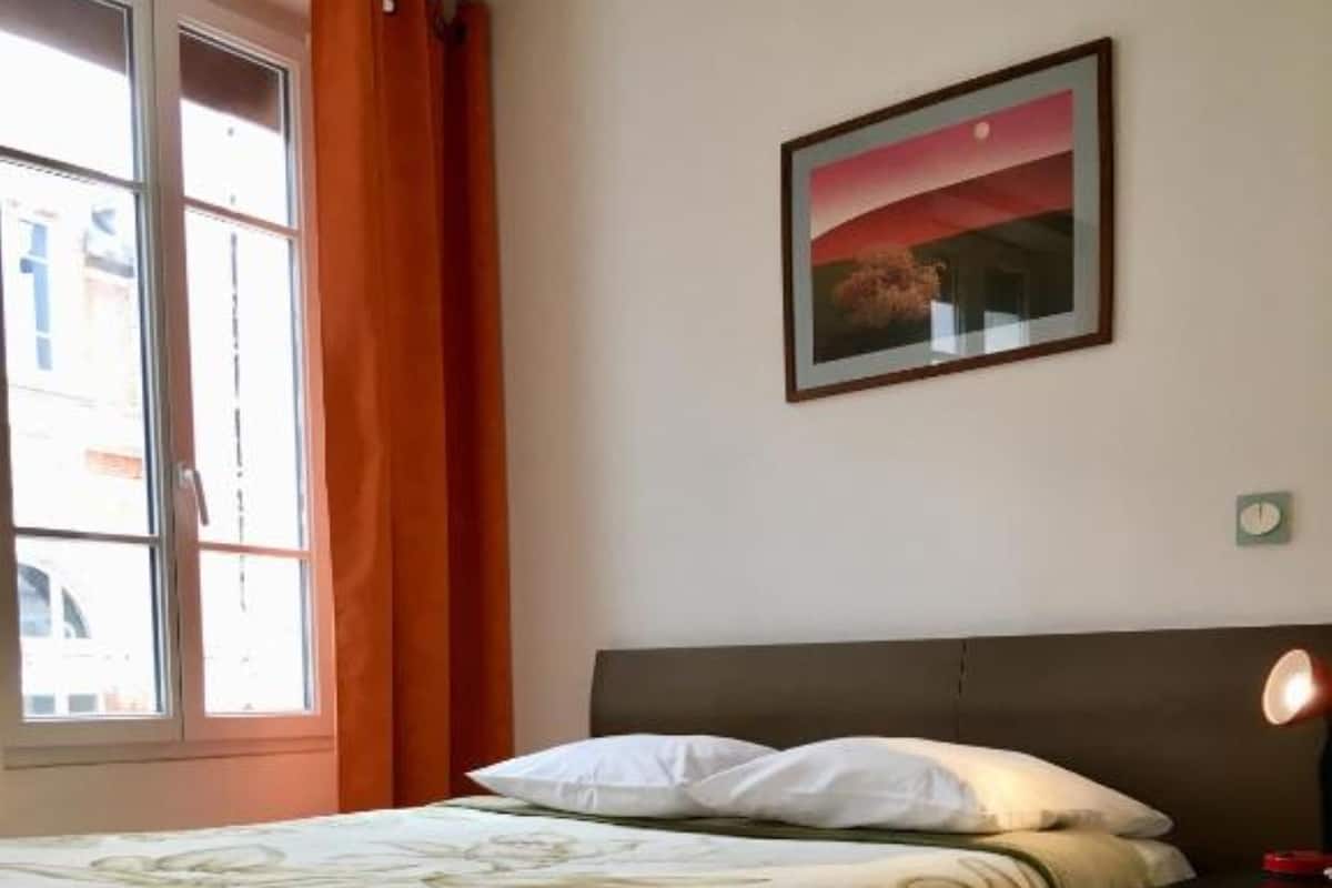 Un dormitorio con cama, mesita de noche, reloj de pared y ventana con cortinas.