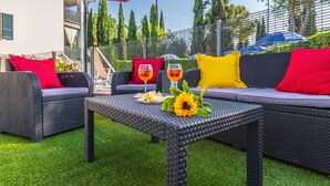 Zona relax esterna con sedute in vimini, un tavolo, cuscini rossi e gialli e una decorazione con girasole.