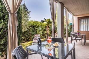 An outdoor patio with a glass table, wicker chairs, a drink, and a menu.
