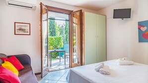 Una camera d'albergo con un letto, un divano con cuscini colorati, una TV e una porta scorrevole in vetro che dà su un balcone.