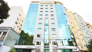 Un hôtel moderne à la façade en verre, appelé « Scorial Rio Hotel », qui se distingue par son entrée imposante et la présence de nombreux drapeaux.