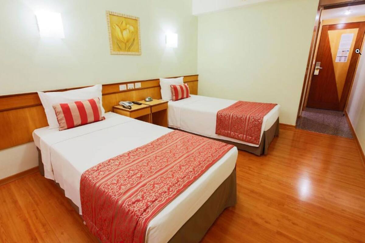 A hotel room with two beds, wooden headboards, a nightstand, a telephone, and a door.