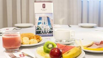 A breakfast setting with a menu box, plates of fruit, pastries, and a glass of juice.