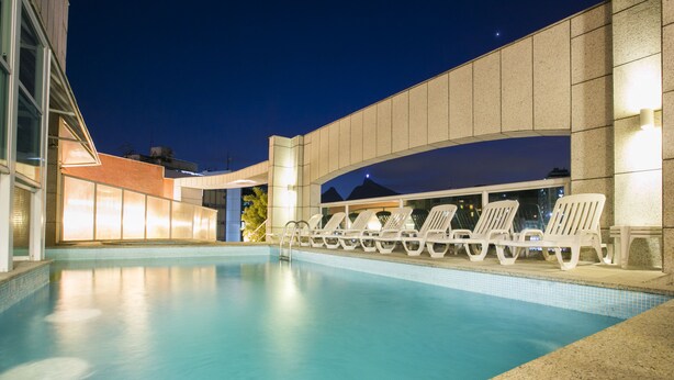 Une piscine avec des chaises longues et un bâtiment dont la façade est recouverte de carreaux.
