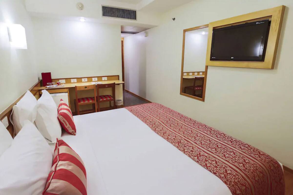 A hotel room with a bed, a desk, a chair, a TV, and a mirror.