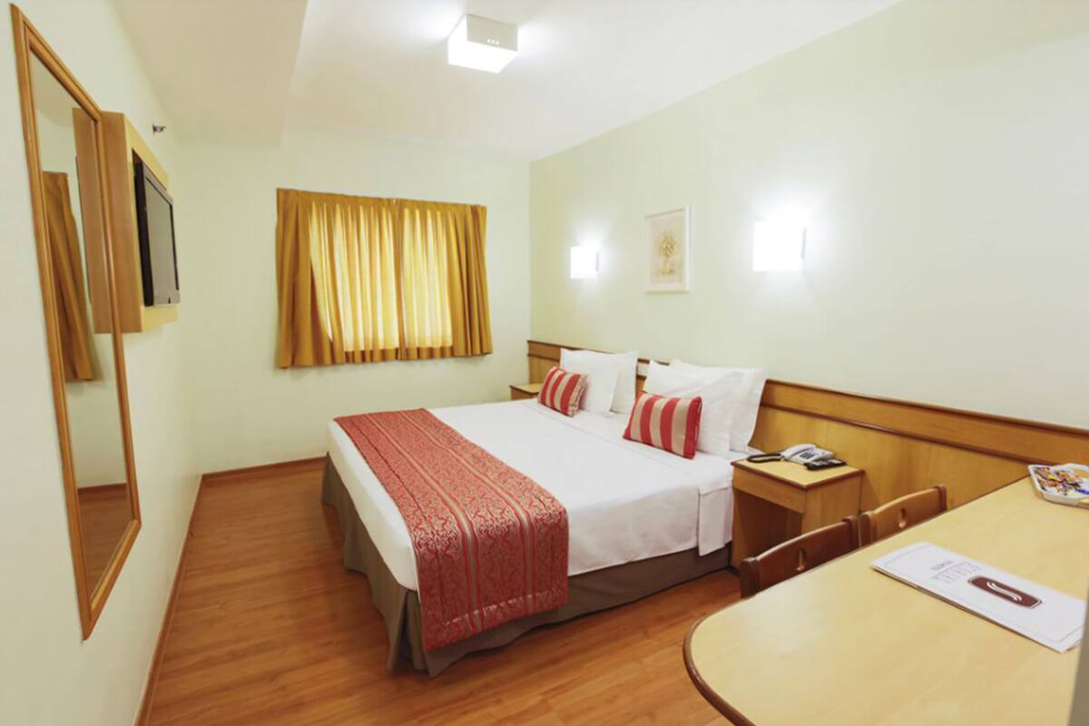 A hotel room with a bed, bedside table, chair, desk, and a mirror.