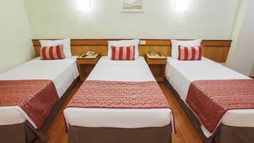 A hotel room with three single beds, each with a red and white patterned bedspread and matching pillows. There are wooden headboards and nightstands with bedside tables.