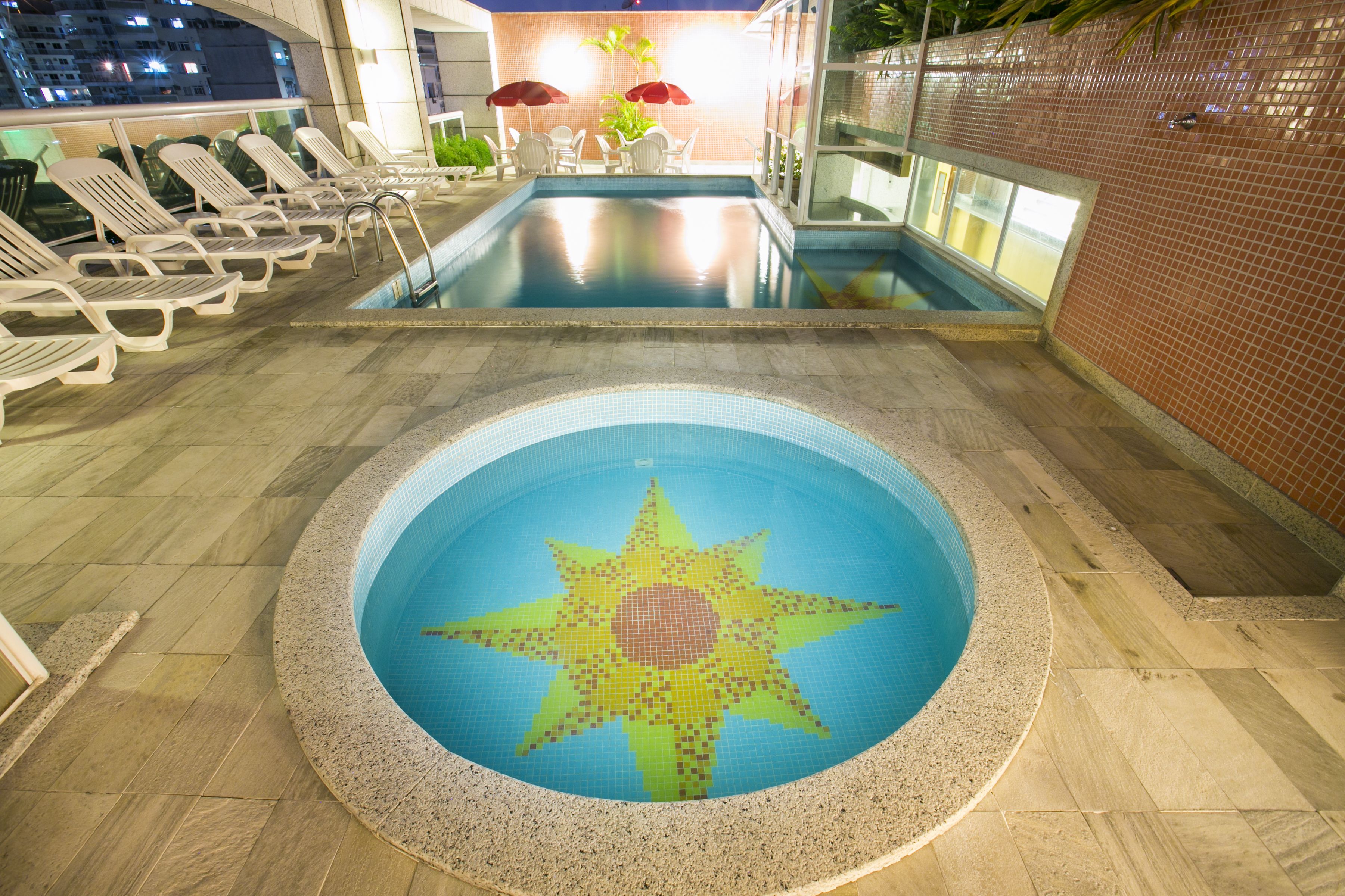 A swimming pool with a star mosaic design, lounge chairs, and a brick wall.