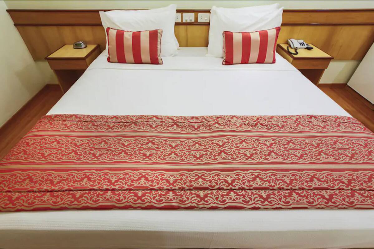 A hotel room with a bed, two nightstands, a telephone, and a patterned red and white bedspread.