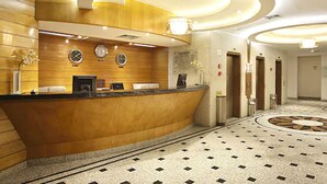 Un hall d’hôtel avec un comptoir d’accueil en bois, plusieurs horloges et un sol à motifs.