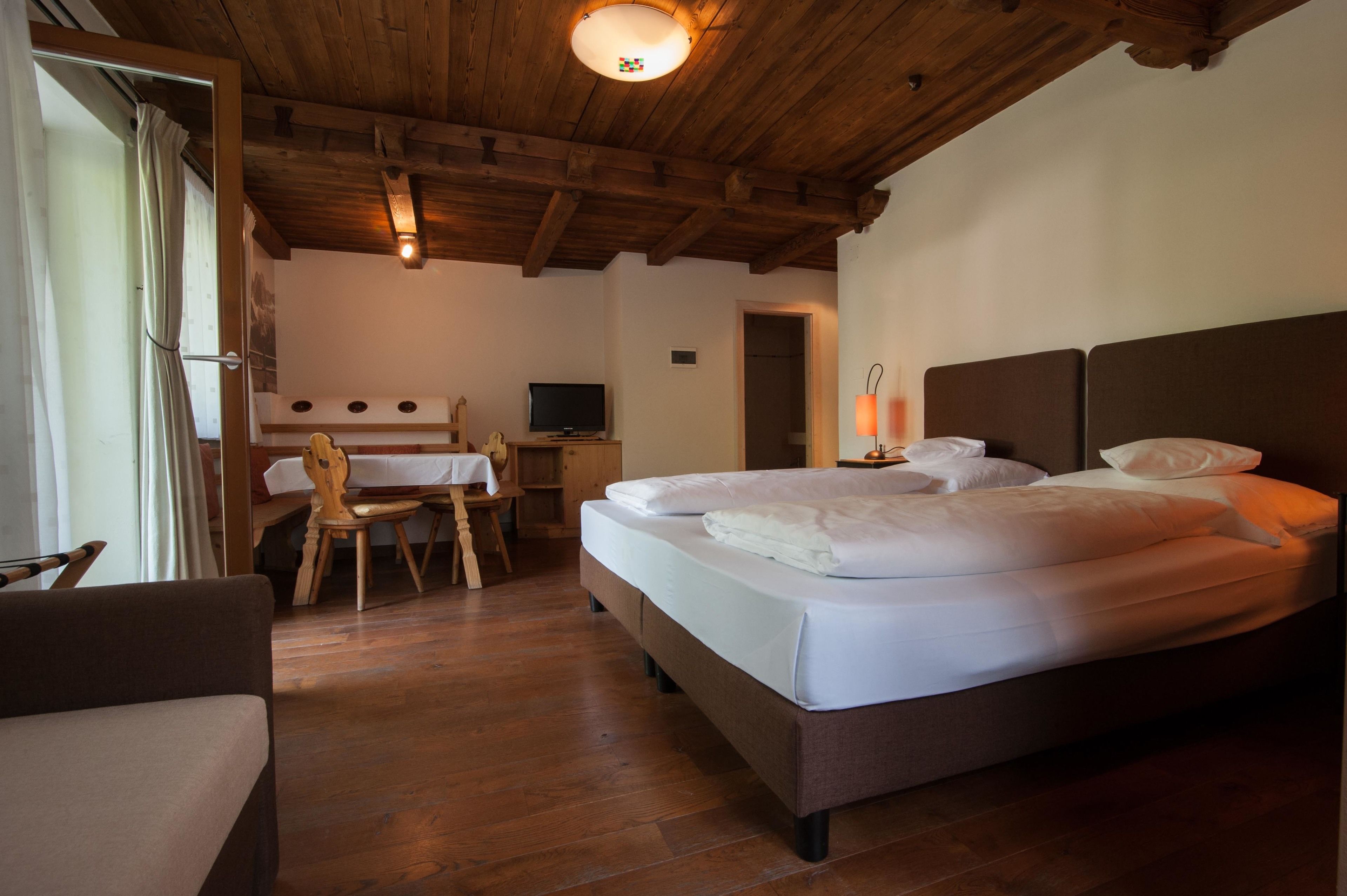 Una habitación de hotel con techo de madera, cama con ropa blanca, escritorio y una silla, y un televisor.