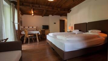 Una habitación de hotel con techo de madera, cama con ropa blanca, escritorio y una silla, y un televisor.
