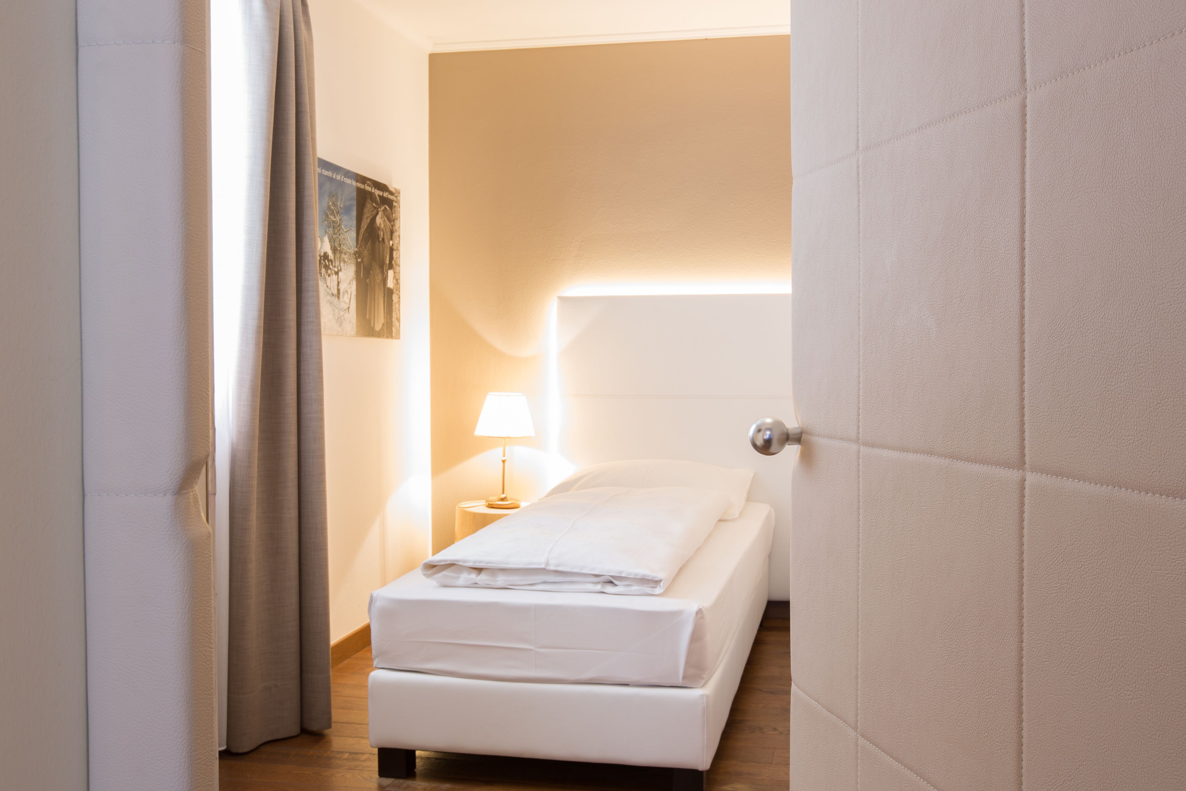 A small, neatly made bed in a room with a wooden floor and a white door.