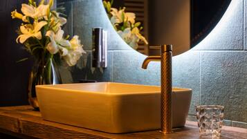 A bathroom with a rectangular sink, a gold faucet, and a vase of white flowers on the counter.